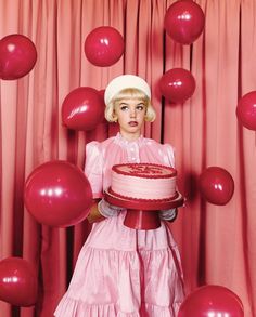 a woman holding a cake in front of balloons