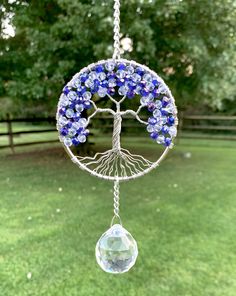 a tree of life with blue flowers hanging from it's side in the grass