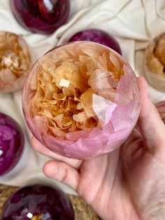 a hand holding a glass ball filled with purple and gold colored objects on top of a table