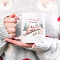 a woman holding a coffee mug with a train on the front and trees on the back