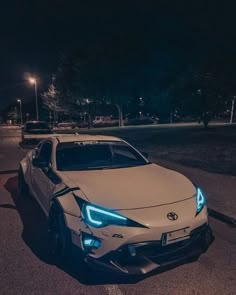 a white car is parked on the side of the road at night time with its lights on