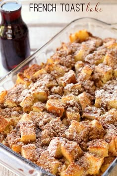 a casserole dish with bread and cinnamon toppings in a glass baking dish next to a bottle of syrup