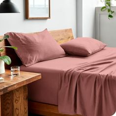 a bed with pink sheets and pillows on top of it next to a wooden table