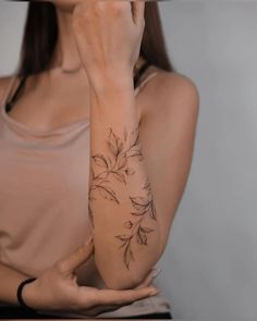 a woman is holding her hand up to her face while she has a flower tattoo on her arm