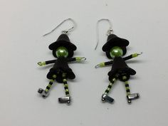 pair of earrings with black and green design on white background, featuring an image of a woman wearing a witches hat