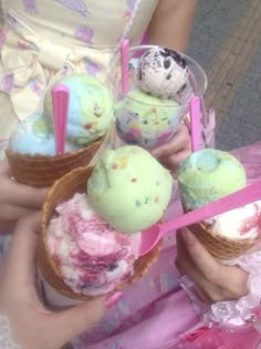 three people holding ice cream cones with pink straws on them and one has an egg in it