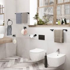 a white bathroom with two toilets and a sink in it's center, along with towels hanging on the wall