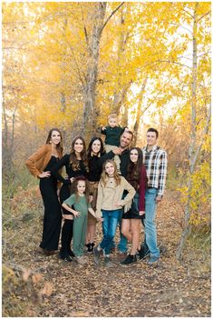 a family posing for a photo in the woods with autumn leaves on the ground and yellow trees behind them