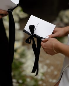 the bride and groom are holding their wedding cards with black ribbon tied around each other