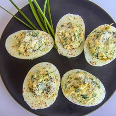 four deviled eggs on a black plate with chives