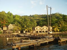 an old wooden dock in front of some houses on the water with palm trees around it