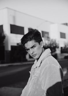 black and white photograph of a young man leaning against a pole on the side of the road