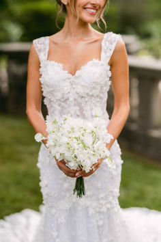 a woman in a wedding dress holding a bouquet of flowers and smiling at the camera