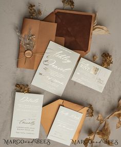 the wedding stationery is laid out on top of brown envelopes and tan paper