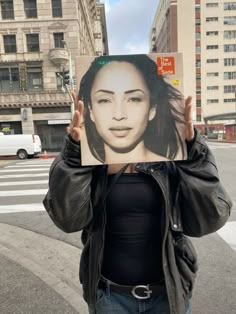 a woman holding up a photo of herself in the middle of the street with her hands