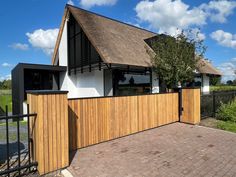 a house with a thatched roof next to a wooden fence and black iron gate