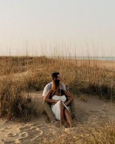 a man and woman sitting in the sand at the beach