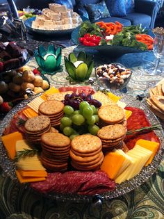 a platter filled with crackers, cheeses and grapes on top of a table