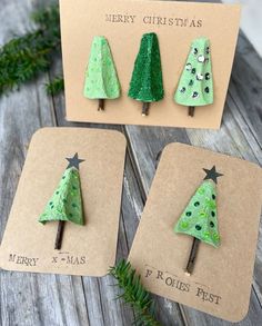 three christmas trees made out of green paper on top of a wooden table next to a card