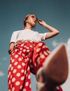 a woman in red and white polka dot skirt looking up into the sky with her hand on her head