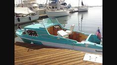 a small blue boat docked at a dock with other boats in the water behind it