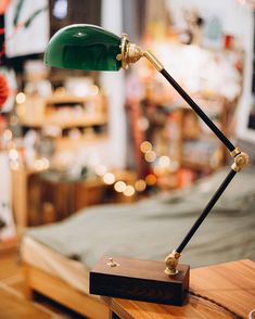 a green desk lamp sitting on top of a wooden table in front of a bed