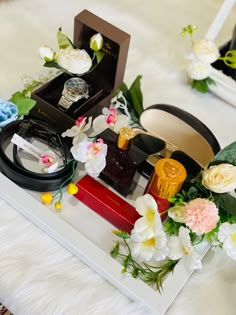 an assortment of perfumes and flowers on a white table with other items in the background