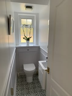 a white toilet sitting under a window next to a sink in a room with tile flooring