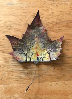 a leaf that has been painted with an image of a person and trees on it