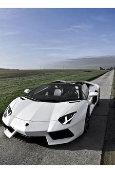 a white sports car parked on the side of a road next to a grassy field