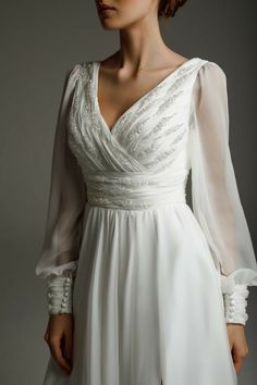 a woman wearing a white dress with long sleeves and beading on the neckline