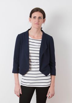 a woman standing in front of a white wall wearing black pants and a striped shirt