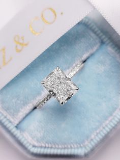 an engagement ring with a princess cut diamond set in a blue velvet box and gold lettering