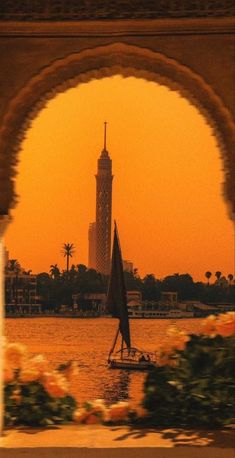 a sailboat is in the water under an arch with a clock tower in the background