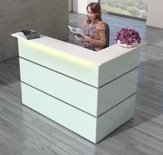 the woman is sitting at the reception desk reading her magazine while holding a cell phone