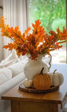 a white vase filled with orange leaves on top of a table next to a pumpkin