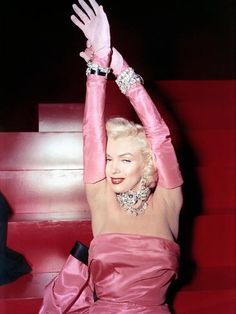 a woman in a pink dress sitting on some steps with her hands up to the ceiling