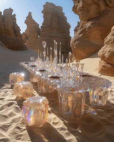 an array of glassware on sand with rocks in the background and sunlight shining through them