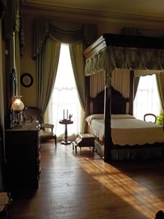 a bedroom with a four poster bed and wooden flooring in front of two windows