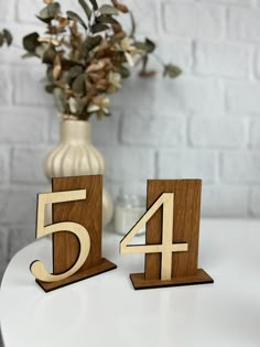 two wooden numbers sitting on top of a white table next to a vase with flowers