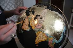 a person is painting the world on a globe with gold paint and black paper machs