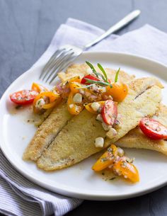 a white plate topped with fish and veggies on top of a blue table cloth