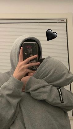 a person wearing a hoodie taking a selfie with a cell phone in front of them