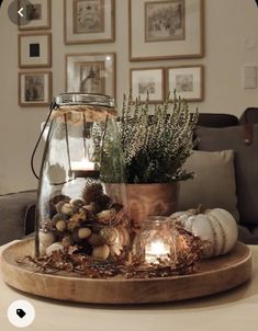 a table topped with a glass vase filled with plants and candles on top of a wooden tray