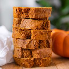 a stack of pumpkin bread sitting on top of a wooden table next to an orange pumpkin