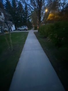 a long sidewalk in the middle of a residential area at night with cars parked on it