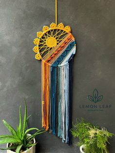 a wall hanging made out of macrame and yarn with a plant next to it