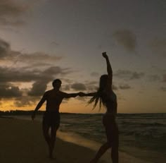 two people are running on the beach at sunset with their arms up in the air