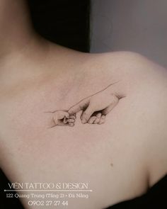 two hands touching each other on the back of a woman's upper shoulder tattoo