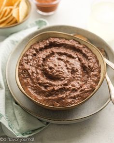 a bowl of chocolate hummus on a plate with chips and drinks in the background